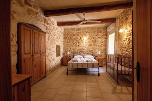 A stone-walled bedroom with a bed, wooden wardrobe, and a ceiling fan.