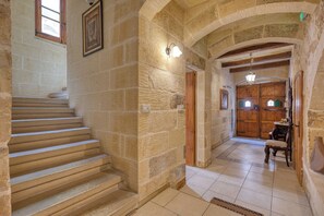 Un escalier en pierre menant à une porte en bois, un sol carrelé et un plafond en bois avec des poutres apparentes.