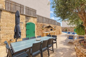 An outdoor patio with a stone wall, a green door, a barbecue area, and lounge chairs by a pool. - Tan Nannu 5BDR Farmhouse in Xaghra by PMI Malta (Ix-Xagħra)