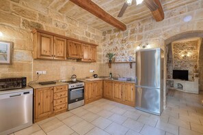 A kitchen with stone walls, wooden cabinets, a stainless steel refrigerator, and a built-in oven. - Tan Nannu 5BDR Farmhouse in Xaghra by PMI Malta (Ix-Xagħra)