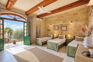 A room with two beds, a ceiling fan, stone walls, and a view of the outdoors. - Tan Nannu 5BDR Farmhouse in Xaghra by PMI Malta (Ix-Xagħra)