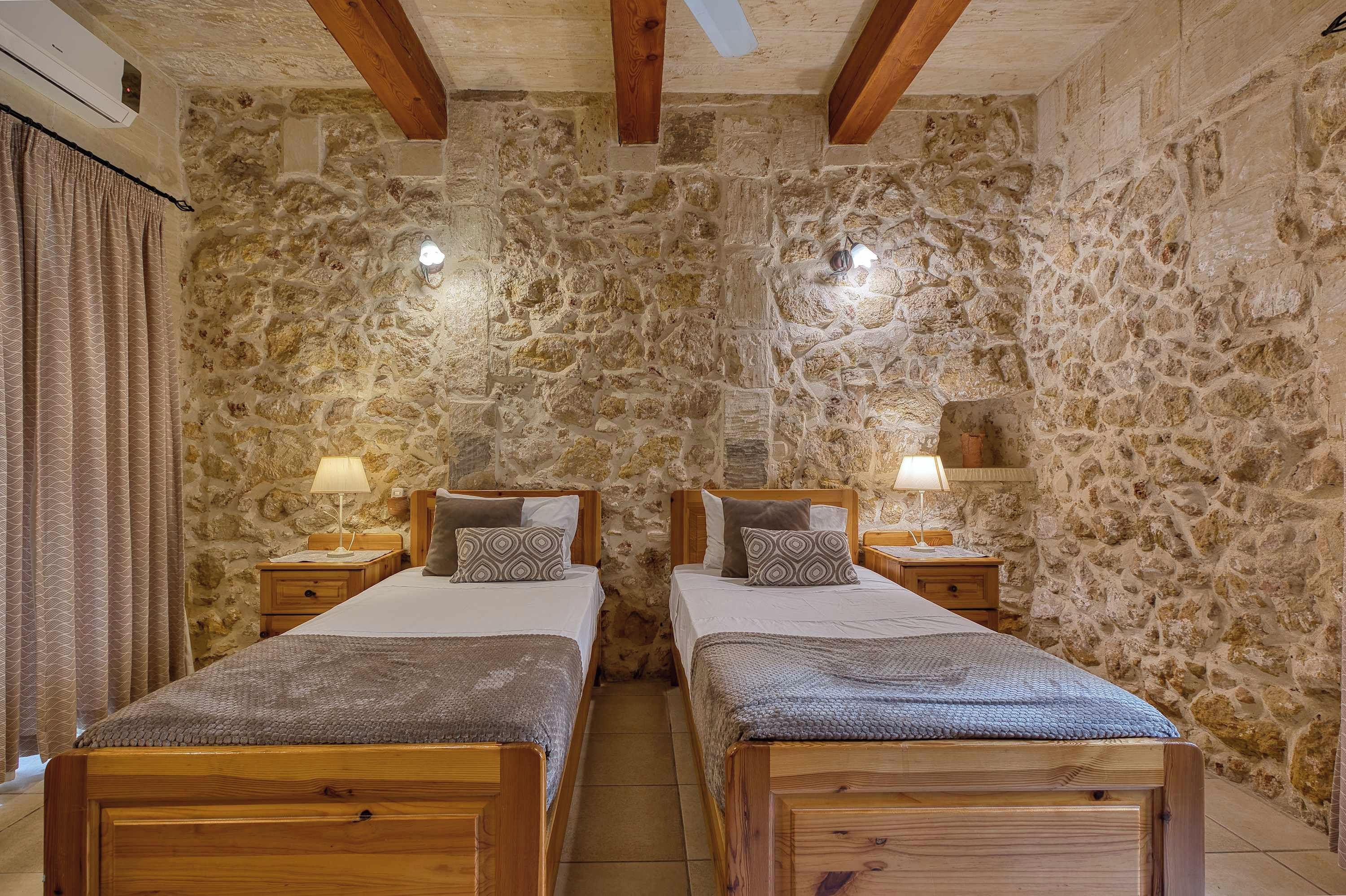 Una habitación con dos camas de madera, paredes de piedra y techo con vigas a la vista.