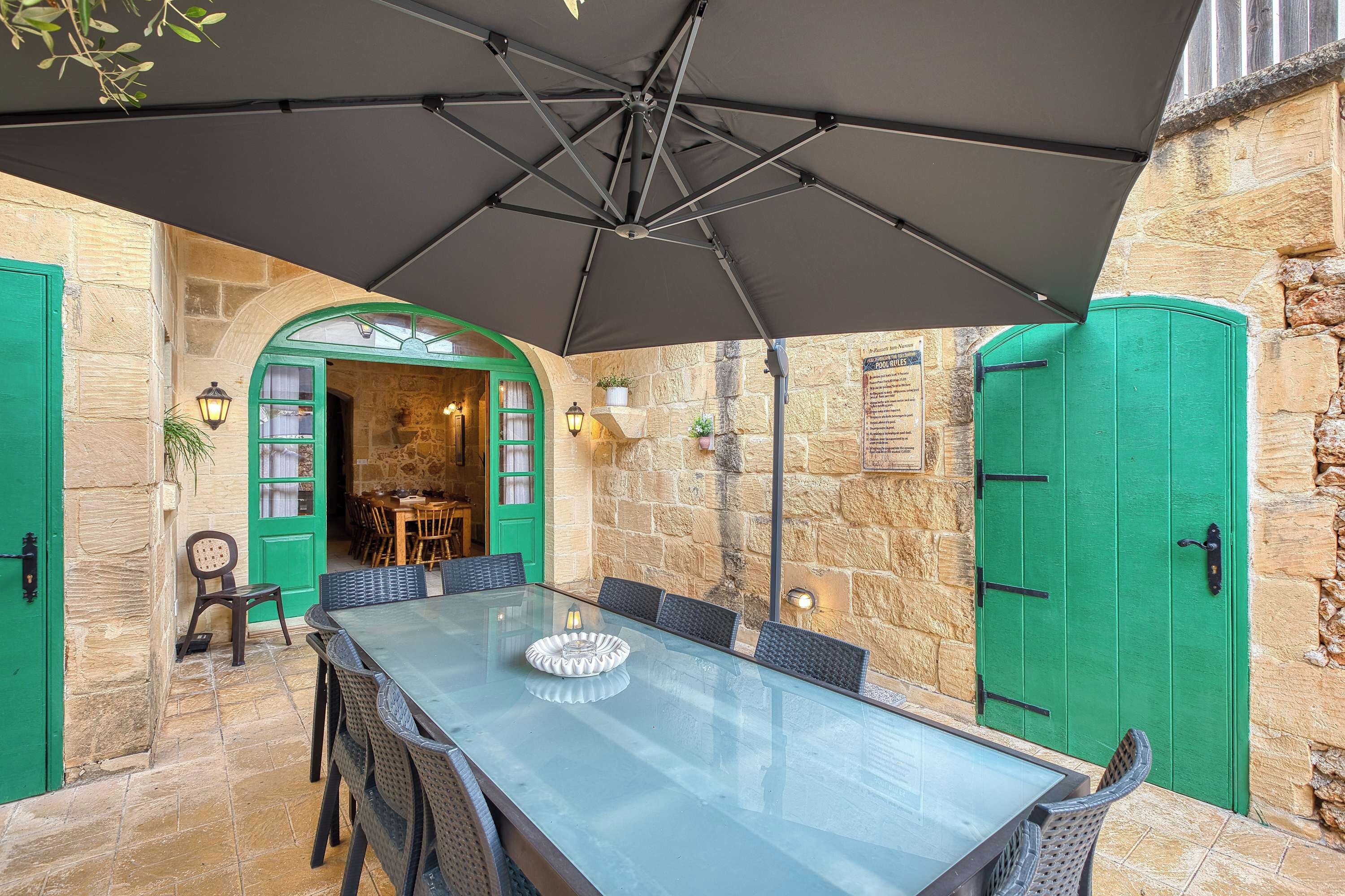 Un coin repas avec une table en verre, des chaises en osier et un grand parasol.