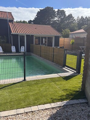 A swimming pool with a tiled deck, surrounded by a fence and a grassy area. - Vacation home with heated pool (Pornic)