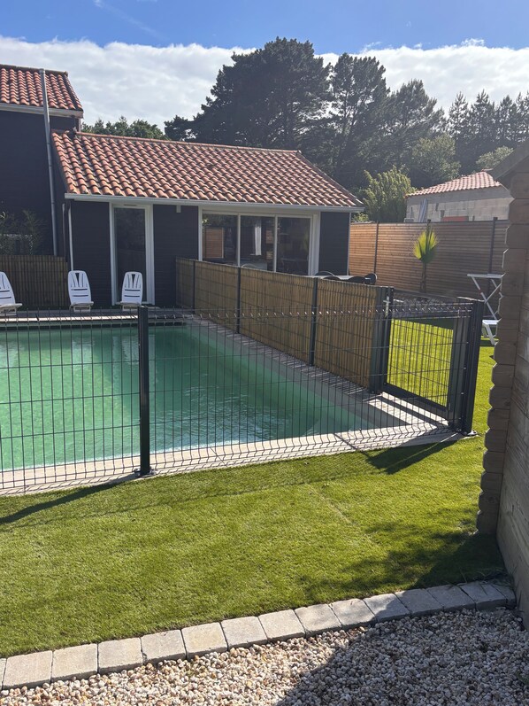 A swimming pool with a tiled deck, surrounded by a fence and a grassy area. - Vrbo Property (Pornic)
