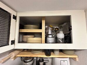A kitchen cabinet with shelves holding plates, bowls, a blender, and a coffee maker.
