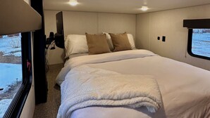 Een slaapkamer met een bed, kussens, een raam en een plafondlamp.