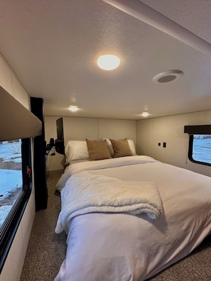 Quarto com cama, almofadas, janela e luminária no teto.