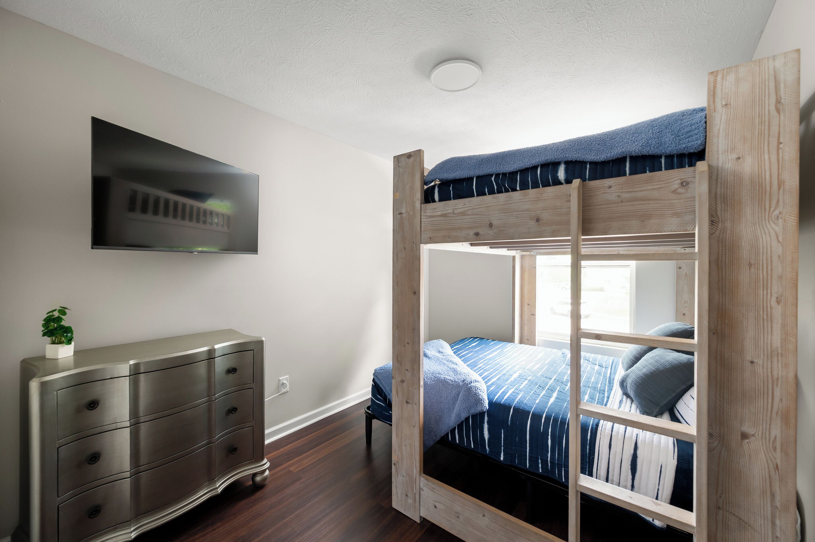 A bunk bed with a TV mounted on the wall, a dresser, and a plant.