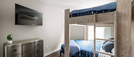 A bunk bed with a TV mounted on the wall, a dresser, and a plant.