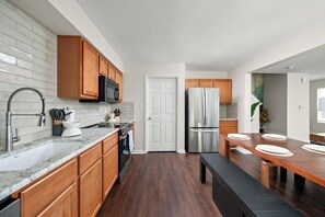 A modern kitchen with wooden cabinets, stainless steel appliances, and a marble countertop. - Modern 4BR  - Townhouse Speedway 11min - Dwntwn 19min, Hot Tub (Indianpolis)