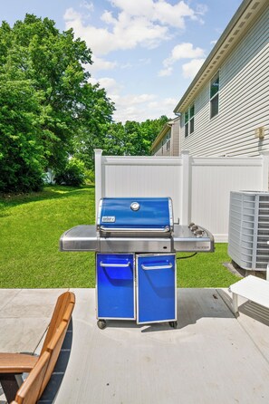A blue Weber grill with a side table and bench, set on a patio with a white fence and green lawn in the background. - Modern 4BR  - Townhouse Speedway 11min - Dwntwn 19min, Hot Tub (Indianpolis)