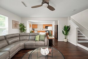 Ein modernes Wohnzimmer mit einer gebogenen Ledersofa, einem Glastisch und einem Deckenventilator.