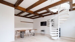 Een modern interieur met een houten plafond, een spiltrap, een eethoek met een tafel en stoelen, en een aan de muur bevestigde televisie.