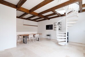 Un interior moderno con techo de madera, una escalera de caracol, un comedor con mesa y sillas, y un televisor instalado en la pared.