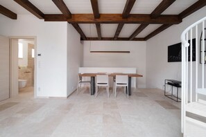 Un intérieur moderne avec une table et des chaises en bois, un plafond blanc avec des poutres apparentes et un sol carrelé.