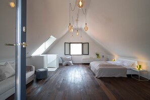 A modern bedroom with a sloped ceiling, a skylight, a bed, a bedside table, and a chair.