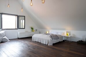 Un dormitorio con cama, mesitas de noche, cómoda, ventana y lámparas colgantes.