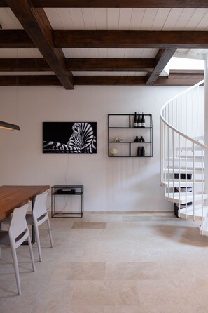 A modern interior with a wooden ceiling, a white staircase, a dining area with chairs, a TV mounted on the wall, and a wine rack.