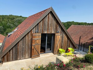 Un edificio de estilo granero de madera con techo inclinado, una puerta de madera grande y un patio con sillas.