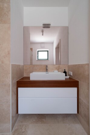 Un baño moderno con un lavabo rectangular, un espejo encima y una encimera de madera.