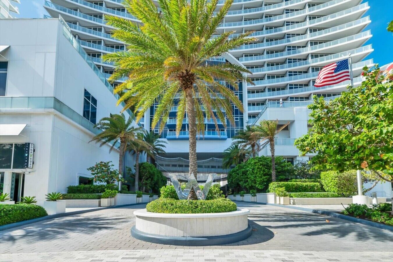 A modern hotel with a central courtyard, palm trees, and an American flag.