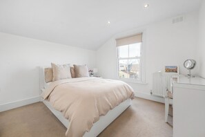 A bedroom with a bed, a window, a radiator, and a desk with a mirror.