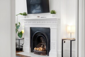 A fireplace with a TV above it, a small plant, and a table with a lamp.