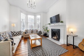 Ein Wohnzimmer mit einer Couch, Couchtisch, Kamin, Fernseher und einer Gitarre.