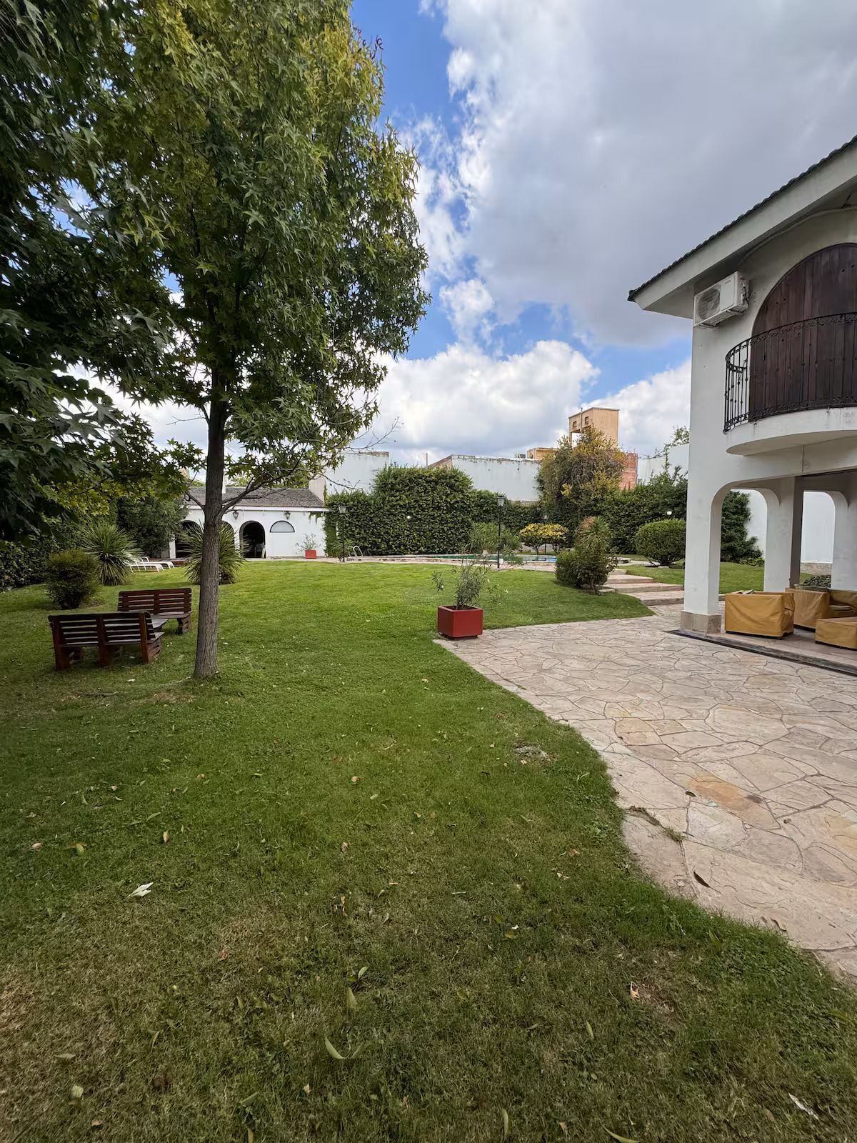 Un patio con césped, bancos, un árbol y un edificio con balcón.