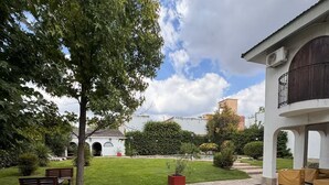 Un cortile con prato, panchine, un albero e un edificio con un balcone.
