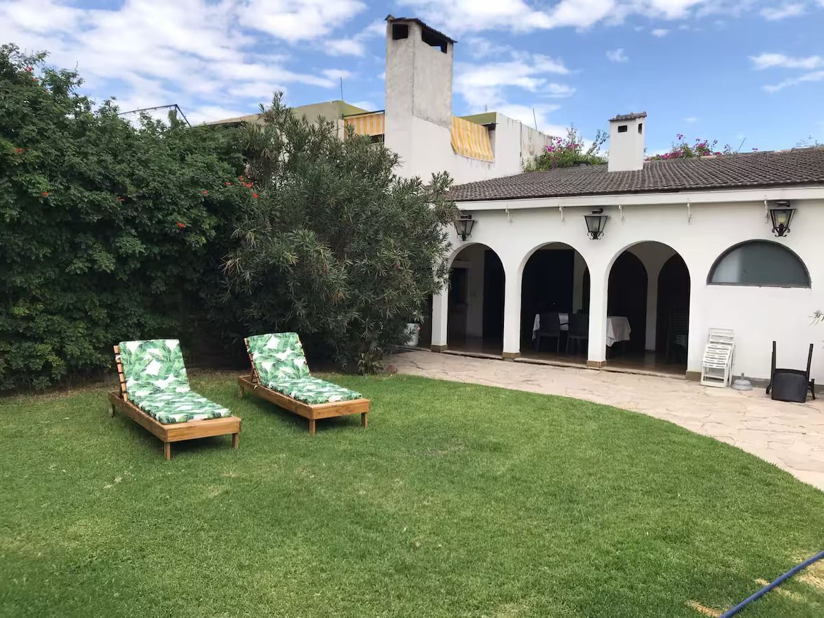A courtyard with two wooden lounge chairs, a white building with arches, and a green lawn.