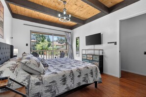 Een slaapkamer met een groot bed, een televisie, een balkon en een houten plafond.