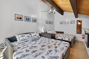 Ein Schlafzimmer mit einem großen Bett, zwei Einzelbetten, einer Kristallleuchter, gerahmten Bildern an der Wand und einer Holzbalkendecke.
