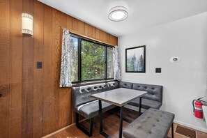 Ein Zimmer mit einer Holzwand, einer Sitzbank mit Tisch, einem Fenster mit Vorhängen, einem gerahmten Bild und einem Feuerlöscher.