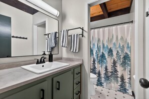 Ein Badezimmer mit Waschbecken, Spiegel und einer Duschvorhang mit Waldmuster.