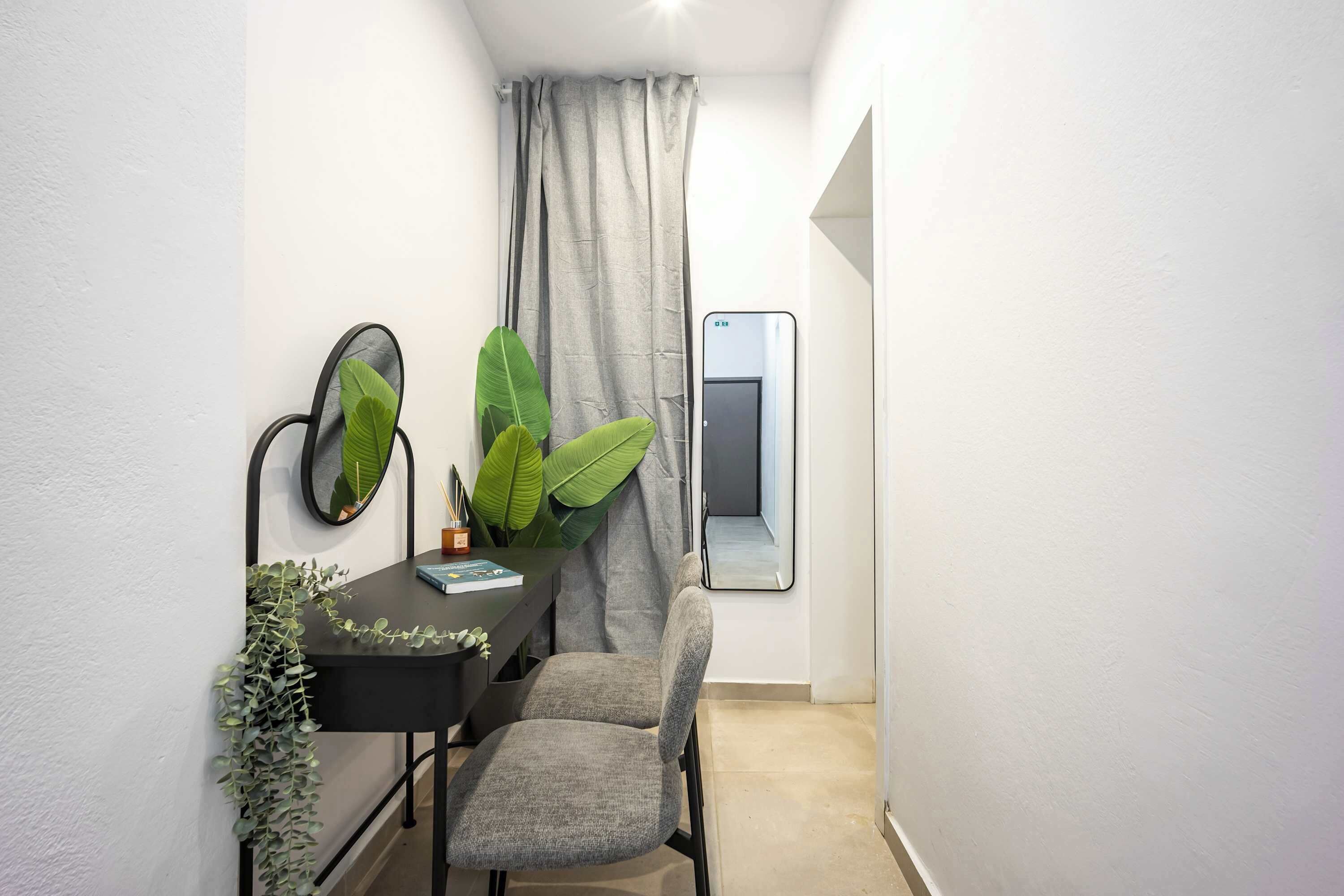 Una habitación pequeña y estrecha con un escritorio, una silla y plantas verdes grandes.