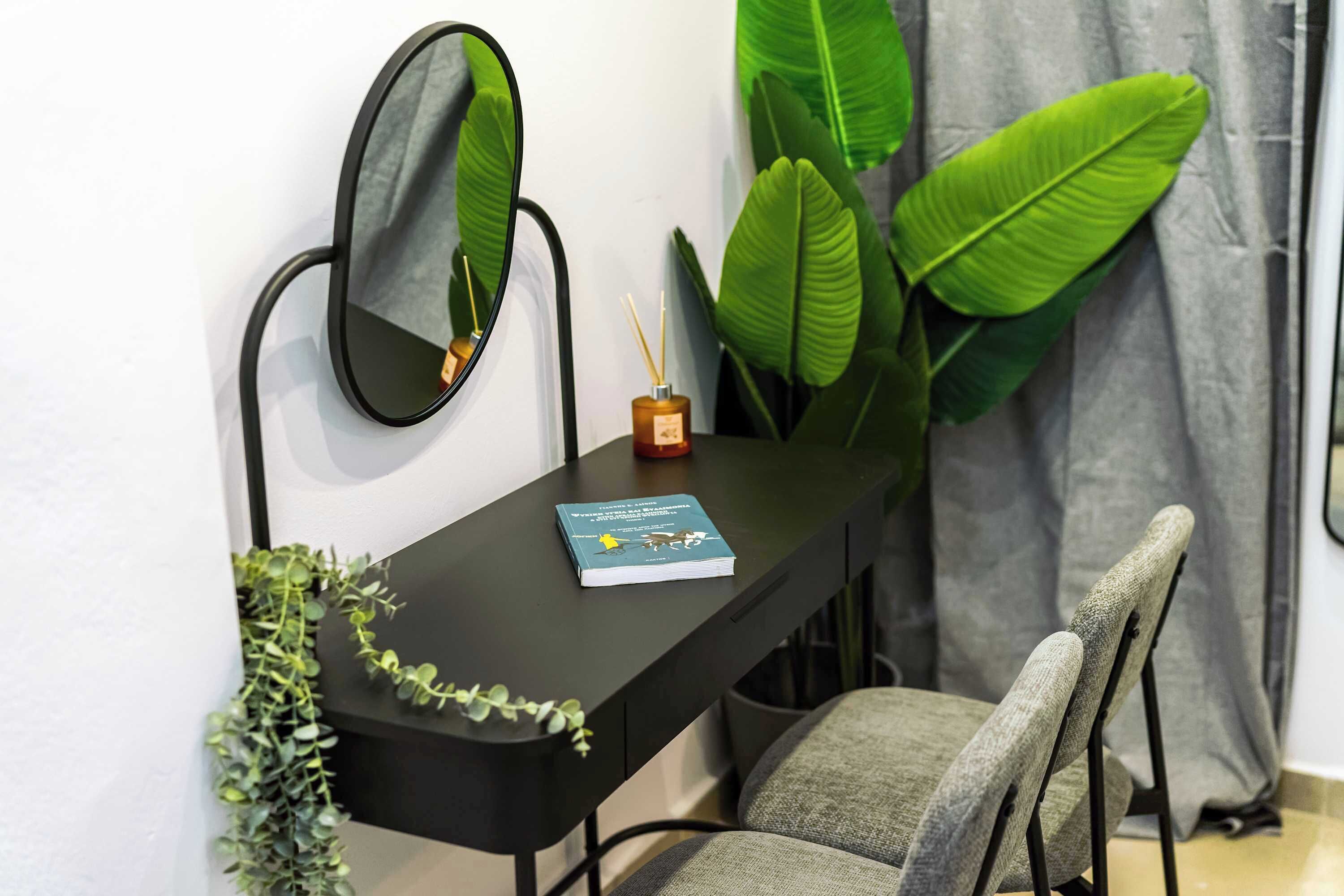 A modern dining area with a black table, two chairs, a mirror, a book, and a small vase with reed sticks.