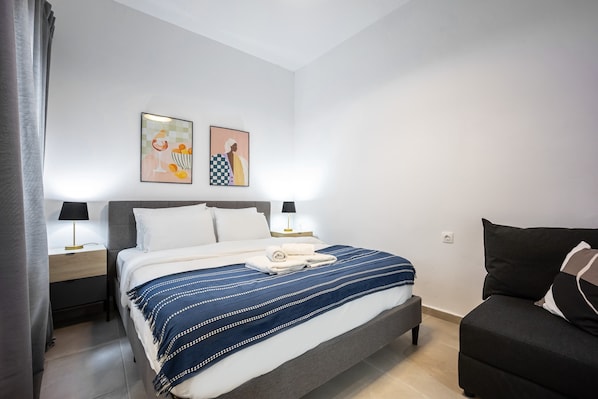Ein modernes Schlafzimmer mit einem Bett, zwei Nachttischen, einem Beistelltisch, einer Couch und zwei Wandbildern.