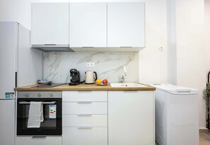 A kitchen with white cabinets, a marble backsplash, a built-in oven, a coffee maker, and a washing machine. - Modern Studio l King Bed & Work Corner (Vironas)