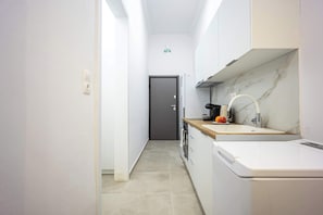 Uma cozinha estreita com armários brancos, painel de fundo de mármore e uma máquina de café.