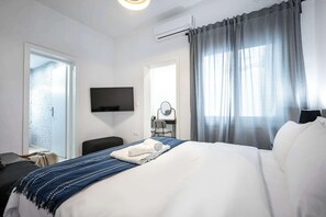 Quarto de hotel com cama, escrivaninha, cadeira, televisão e janela com cortinas.