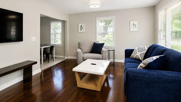 A living room with a TV, a sofa, a coffee table, and a dining area with a table and chairs.
