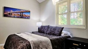 A bedroom with a bed, a skylight, a cityscape painting, and a window with blinds.