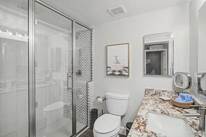 A bathroom with a shower, toilet, sink, and a framed picture on the wall.
