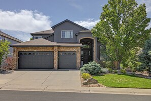 A two-story house with a stone facade, two garage doors, and a well-maintained front yard with a tree and shrubs. - Luxury Mountain View Retreat in Castle Pines (Castle Pines)