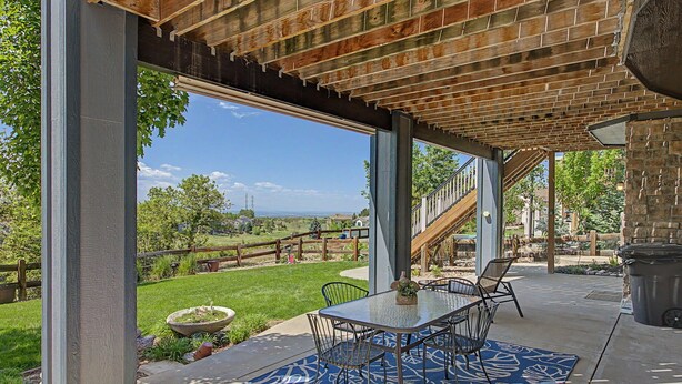 Un patio al aire libre con una mesa y sillas, vista a un espacio cubierto de césped y una valla de madera.