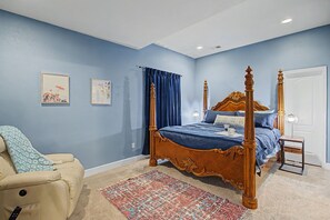 A bedroom with a four-poster bed, a small bedside table, a chair, and a patterned rug.