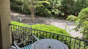 Ein Balkon mit Tisch und Stühlen, der auf einen Garten mit Bäumen und einem Wasserspiel blickt.