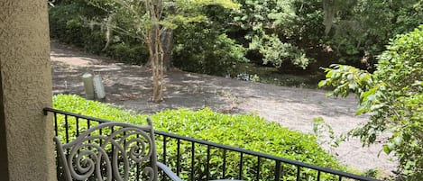 A balcony with a table and chairs, overlooking a garden with trees and a water feature.